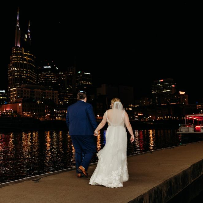 Bride and Groom walking along riverfront in Nashville with Skyline at night