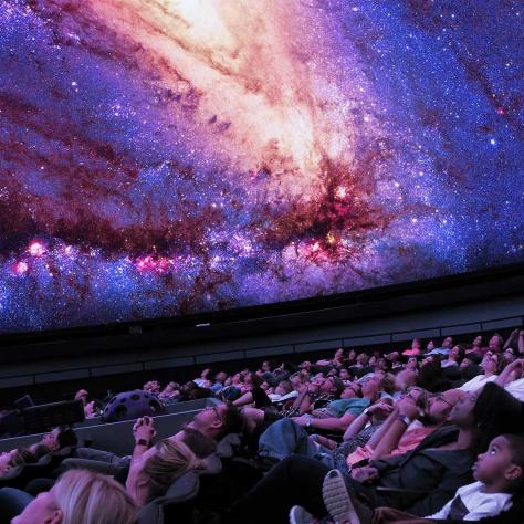 A crowd looking up at stars on the ceiling of a planetarium