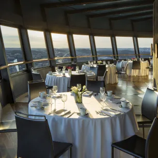 Restaurant dining area with round tables and panoramic city views at sunset