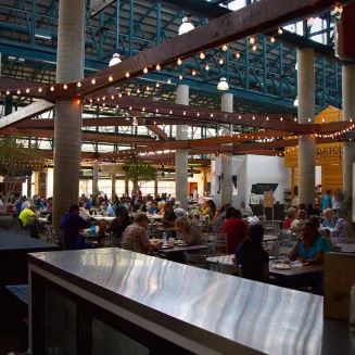 People eat at tables in a large indoor dining area at the Nashville Farmers' Market in Nashville, Tennessee.