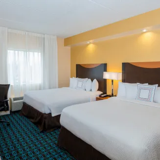 Hotel guest room with two double beds, desk, and window with sheer curtains.