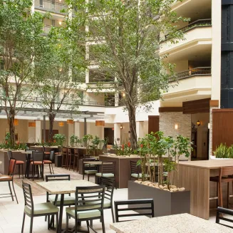 Hotel atrium dining area with tall indoor trees, tables and chairs, and multi-story balconies.