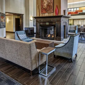 Hotel lobby lounge with sofas and armchairs arranged around a fireplace on wood floors.