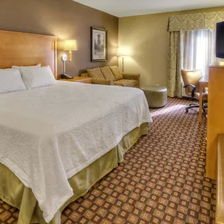 Standard king room with bed, sofa, desk and TV in warm neutral décor.