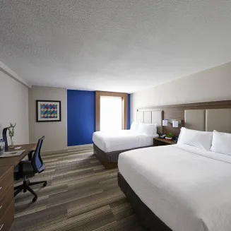 Hotel guest room with two queen beds, desk, and flat-screen TV