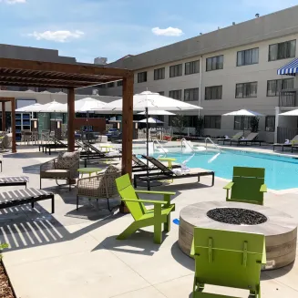 Hotel outdoor pool area with lounge chairs, umbrellas, and fire pit seating.
