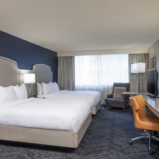 Hotel guest room with two beds, desk, and seating area by the window.