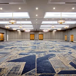 Spacious hotel ballroom with patterned carpet, chandeliers, and skylights.