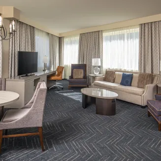 Hotel suite living area with sofa, armchairs, dining table, and large windows.