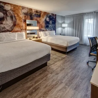 Hotel guest room with two queen beds, artistic wall mural, and modern furnishings.