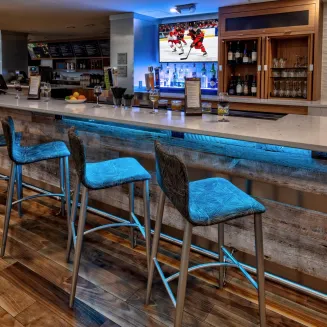 Hotel bar with illuminated counter, barstools, and televisions showing sports.