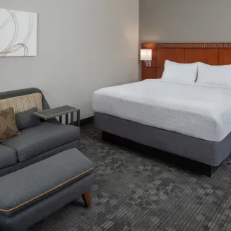 Hotel guest room with king bed, sofa, and modern decor.