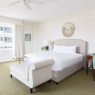 Bright deluxe room with king bed, chaise bench, writing desk, and soft neutral palette.