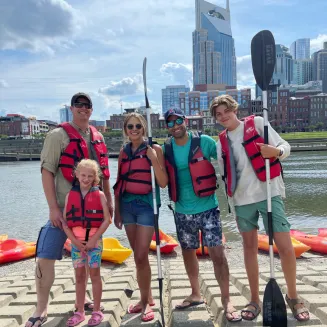 Family of kayakers pose in front of Nashville skyline. Nashville, TN.