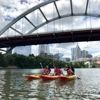 Friends pose in kayaks on the Cumberland River with the Nashville skyline in the background. Nashville, TN.
