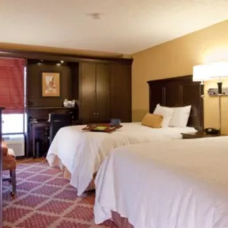 Hotel guest room with two beds, desk, and warm lighting.