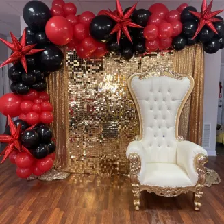 Gold and white rental throne chair in front of gold shimmer wall accented with balloons and LED sign
