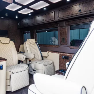 The 6-7 Passenger Mercedes Jet Sprinter interior features plush leather captain’s chairs, woodgrain flooring, ambient LED lighting, and a spacious cabin.