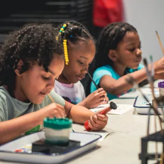 Three young children making art at a painting station