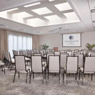 Hotel meeting room with rows of chairs facing a presentation screen and podium.