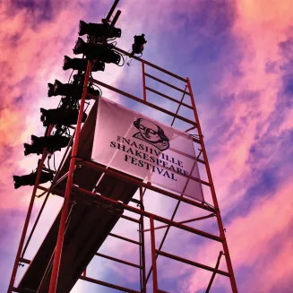 Nashville Shakespeare Festival logo banner on light tower with sunset